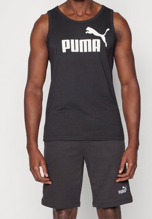 Mand iført sort Puma ærmeløs top og matchende sorte Puma shorts, stående mod en ensfarvet baggrund.