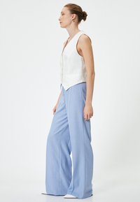 Gilet bianco in lino con scollatura a V e bottoni frontali, abbinato a pantaloni a gamba larga blu chiaro realizzati in un tessuto texture.