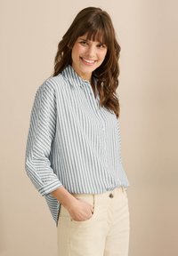 Camicia a maniche lunghe a righe blu chiaro e bianca con colletto, orlo arrotondato, abbinata a pantaloni chiari.
