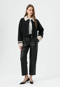 Zwarte cropped jas met een crème faux fur kraag en manchetten, gecombineerd met zwarte high-waist leren broeken en puntige zwarte hakken.