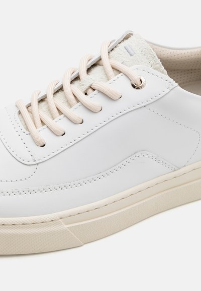 Weißes Leder-Sneaker mit hellbeigen Akzenten, flachen Schnürsenkeln und einer strukturierten Gummisohle. Die Steppnähte an der Seite verleihen dem Design zusätzlichen Charme.