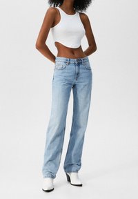 Jeans de mezclilla azul claro con corte recto, que cuentan con cinco bolsillos y detalles de costura sutiles. Llevado con una camiseta corta blanca y botas de tacón.