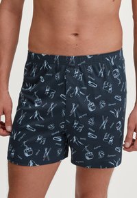 Donkerblauwe boxershorts met een patroon van skirelevante iconen en Zwitserse namen, gemaakt van zacht, ademend materiaal met een elastische tailleband.
