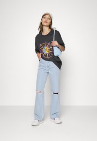 T-shirt cinza oversized com um gráfico de sol, jeans rasgados em azul claro e ténis brancos. Os acessórios incluem uma mala de ombro azul claro e um boné.