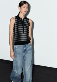 Svart och vit randig ärmlös topp med krage, parat med löst sittande ljusblå denimjeans. Toppen har en knappslå.