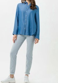 Jasnoniebieska koszula dżinsowa z długimi rękawami, zapięciem na guziki z przodu oraz zaokrąglonym hemem. Połączona z jasnoniebieskimi spodniami o tapered fit i białymi trampkami.