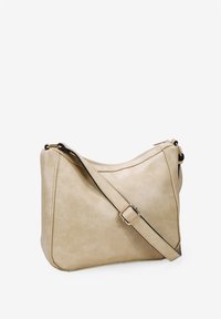 Bolso cruzado de piel sintética beige con una textura suave, forma curva, correa ajustable y detalles en tono dorado.