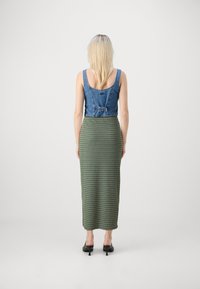 Denim odrezan top z zaobljenim izrezom, v kombinaciji z dolgo zeleno progasto krilo. Črne sandale z visoko peto dopolnjujejo to obleko.