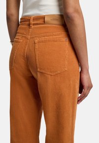 Oranje corduroy broek met verticale ribbelstructuur, met achterzakken en een leren label op de tailleband.
