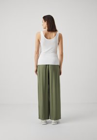 White tank top paired with loose-fitting, olive green wide-leg pants, featuring a smooth texture and worn with white sneakers.