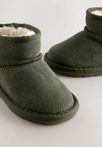 Dunkelgrüne Wildleder-Stiefeletten mit einem weichen Fellfutter und einer strukturierten Gummisohle. Mit dekorativen Nähten um das obere Teil.