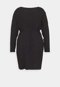 Vestido preto com nervuras, mangas longas, decote redondo e um cinto a condizer na cintura. O tecido tem uma textura suave e um padrão vertical.