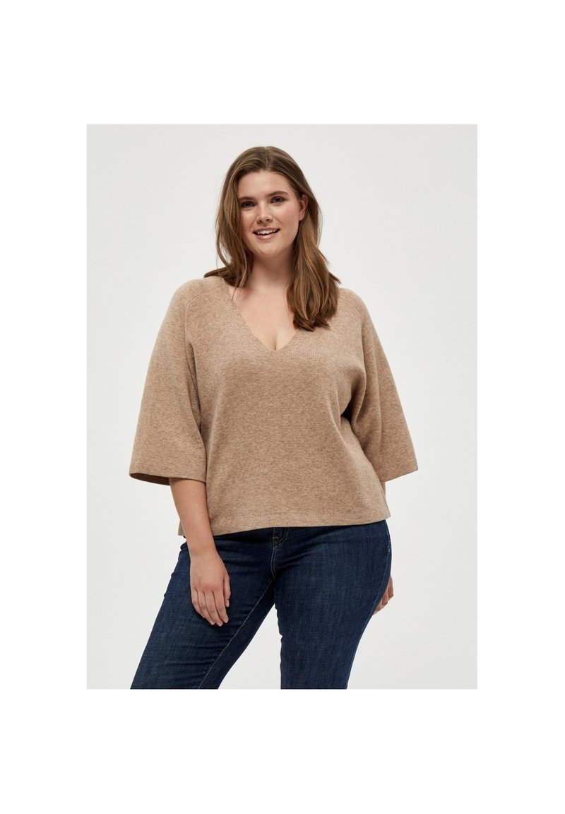 Beige oversized sweater met een V-hals, korte wijde mouwen en een zachte, textuurrijke afwerking. Gecombineerd met donkere jeans.