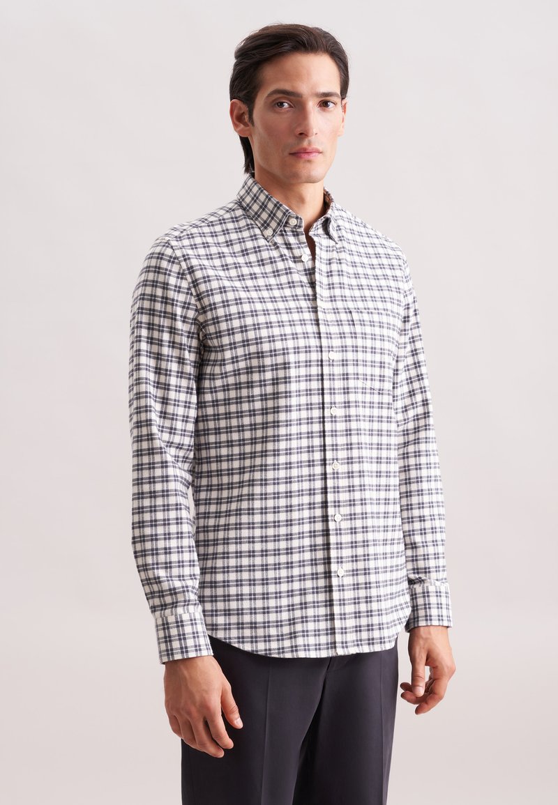 Camicia a maniche lunghe bianca con motivo a scacchi blu e neri. Design con colletto e tasca frontale. Tessuto morbido.