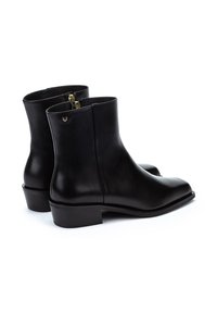 Botas de tobillo de cuero negro con un acabado suave, punta redondeada, tacón bajo de bloque y un sutil herraje dorado en la cremallera.