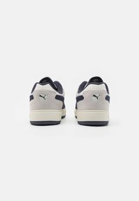 Sneakers grigio in suede con accenti blu navy, colletto imbottito e suola in gomma bianca. Logo sul tallone e sul lato, design minimalista.