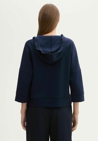 Sweat à capuche bleu marine avec un bord de capuche froncé, des manches trois-quarts et une coupe décontractée, fabriqué à partir d'un tissu lisse et léger.