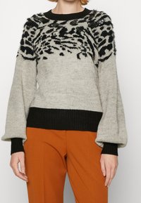 Gray knit sweater with a black animal print design at the top, featuring a ribbed black hem and long, puffy sleeves. Paired with orange trousers.