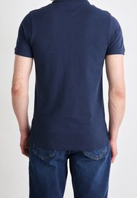 Navy blue polo shirt made of smooth fabric, featuring a classic collar and short sleeves. Worn with denim jeans, showcasing a simple design.