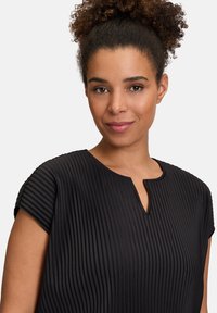Schwarzes Plissee-Top aus einem weichen Stoff, mit kurzen Ärmeln und einem Schlitz-Ausschnitt. Glatte Textur und vertikale Linien im gesamten Design.
