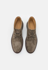 Bruna mockaskor som går till anklarna med en slät textur, rund tå, två öglor och en kontrasterande beige insida. Gummisula med sydda detaljer.