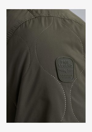 Chaqueta verde acolchada con una superficie texturizada, detalles de costura redondeados y un parche de goma negro con la etiqueta "PME LEGEND AMERICAN CLASSIC."