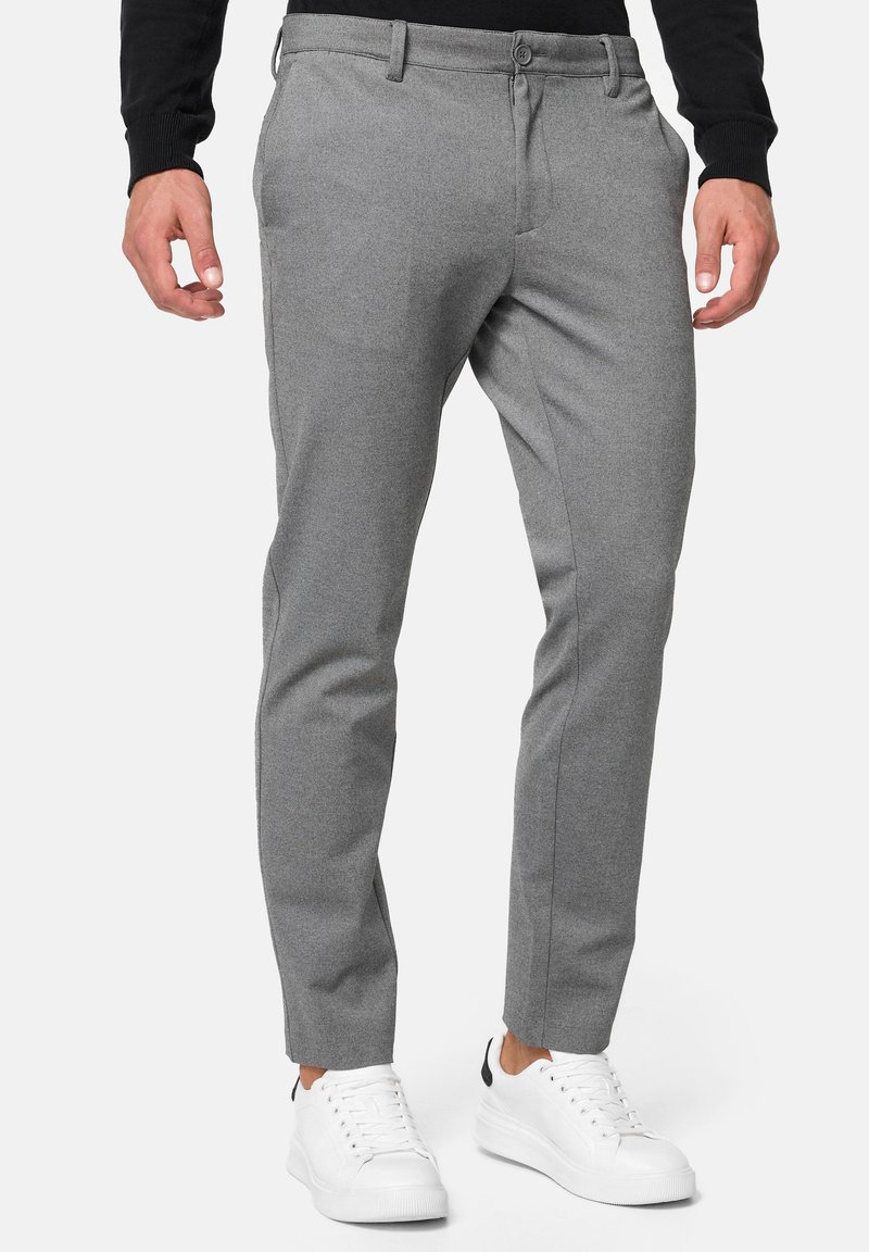 Pantalones de vestir gris ajustados, fabricados con una tela texturizada, cuentan con un cierre de botón, bolsillos laterales y están combinados con zapatillas blancas.