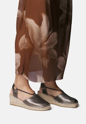 Metalen zilveren sleehak-espadrilles met gevlochten jutezolen. Voorzien van een open achterkant, gekruiste bandjes en een gladde, glanzende textuur.