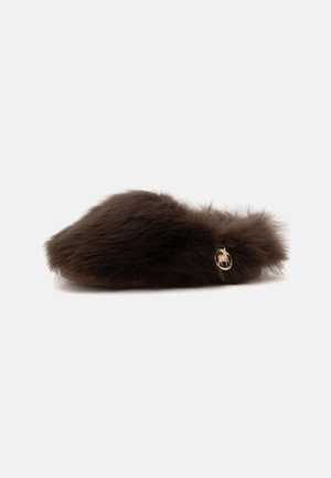 Chausson marron foncé en peluche à enfiler avec une texture douce en fourrure et un petit charm doré rond sur le côté.