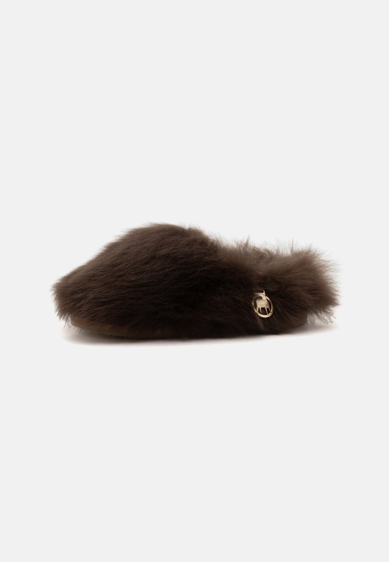 Chausson marron foncé en peluche à enfiler avec une texture douce en fourrure et un petit charm doré rond sur le côté.