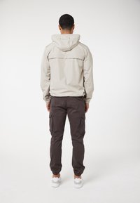 Ljusbeige luvjacka med söm i bakfickan, ihop med mörkgrå cargobyxor med sidofickor; bärs med vita skor.