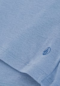 T-shirt di cotone azzurro chiaro con una texture liscia, con orlo cucito e un piccolo logo stampato vicino all'angolo in basso a destra.