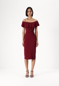 Burgundská off-shoulder šaty s volánovým výstrihom, priliehavý strih, po kolená a s bočným rozparkom, skombinované s čiernymi sandálmi na ihlovom podpätku.
