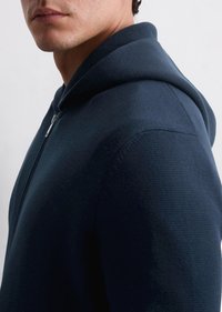 Navy blue zippered hoodie made of textured fabric, featuring a hood and a close-fitting design that emphasizes the collar and shoulder.