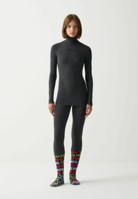 Maglia termica nera aderente con maniche lunghe e collo alto, abbinata a leggings; calzini con fantasia colorata e testo "Colmar" in colori vivaci.