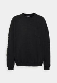 Sudadera negra de algodón con cuello redondo, mangas largas, un bolsillo frontal y texto impreso a lo largo de la manga. Textura suave.