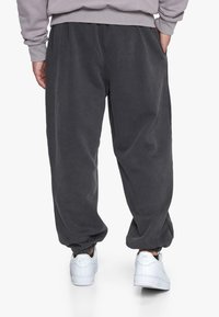 Fleece joggerbukser i mørkegrå, med elastisk talje og manchetter, parret med hvide sneakers, set fra ryggen.
