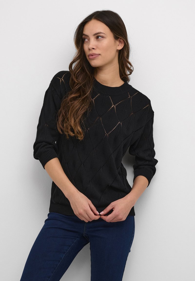 Maglione nero lavorato a maglia con fori a forma di diamante, colletto e polsini a coste, e vestibilità morbida. Abbinato a jeans in denim blu scuro.