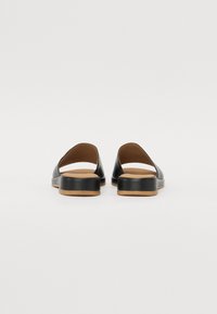 Black slide-on shoes with a low heel, smooth leather upper, open back design, and light tan rubber sole. Simple and modern aesthetic.