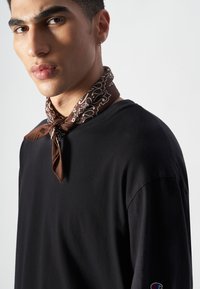 Czarna koszula z długim rękawem wykonana z gładkiego materiału, z okrągłym dekoltem. Na szyi zawiązana brązowa chustka z białymi wzorami.