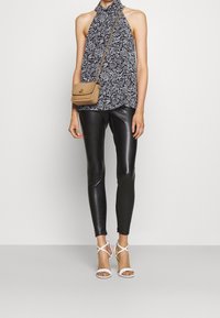 Top de tirantes floral en blanco y negro, leggings de cuero sintético negros y sandalias de tacón alto blancas con tiras. Bolso cruzado de color bronceado con correa de cadena.