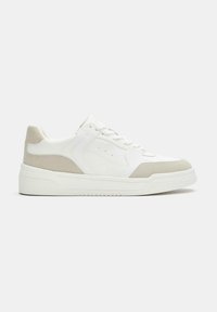 Witte lage sneaker met beige suède accenten op de hiel en neus, veterluiting en dikke rubberen zool, op een effen achtergrond.