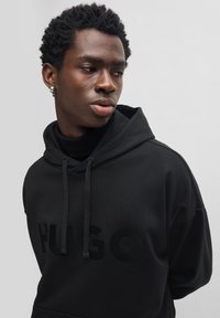 Schwarzer Kapuzenpullover mit großem, strukturiertem "HUGO"-Logo. Ausgestattet mit Kordelzug, weichem Material und lässiger Passform.