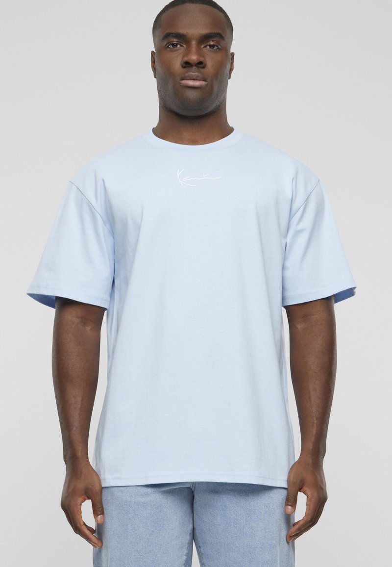 Ανοιχτό μπλε βαμβακερό T-shirt με κοντά μανίκια, που έχει ένα μικρό λευκό λογότυπο στο μπροστινό μέρος. Χαλαρή εφαρμογή με στρογγυλή λαιμόκοψη.