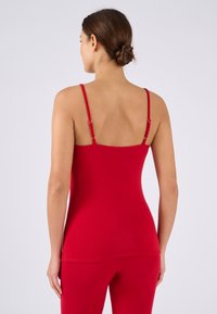 Top rosso senza maniche con spalline sottili, texture liscia e design aderente. Indossato con pantaloni rossi coordinati, che mostrano un look semplice e coerente.