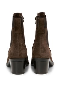 Bottes chelsea en daim marron avec un talon moyen et des panneaux élastiques sur les côtés. Avec un tirette à l'arrière et un talon noir brillant et élégant.