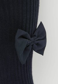 Calze navy lavorate a maglia con una texture a coste e un grande fiocco in tessuto sul lato, che aggiunge un dettaglio al design complessivo.