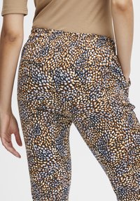 Gemusterte Hose in Orange, Schwarz und Weiß mit strukturierter Oberfläche. Elastischer Bund und Seitentaschen, mit einem gepunkteten Design.