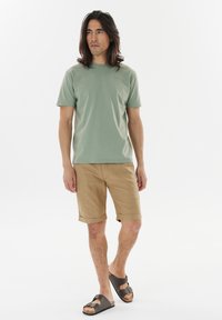 Green short-sleeve t-shirt, khaki shorts with rolled cuffs, and dark brown sandals. The fabric appears smooth and casual in style.