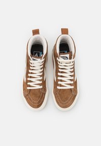 Brune semskede høyhælte sneakers med hvite snøringer, en hvit sidestripe og en svart logo på sålen. Inkluderer en bakre pull-tab for enkel påkledning.